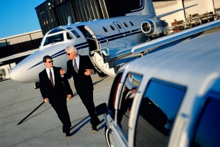 Two man on a suit walking away on airplane and approaching a limousine shuttle.